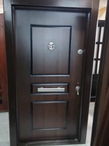 A brown steel security door with a classic design featuring raised panels. The door has a silver letterbox, a round door knocker, and two keyholes.