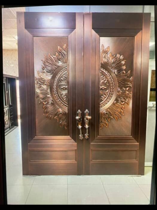 A pair of grand double doors with a bronze finish, featuring intricate floral and sunburst designs. The doors have ornate handles and are set against a tiled floor.