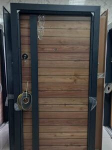 A modern single security door with a black metal frame and horizontal wood grain panels. The door features a keyhole and a ring-shaped door handle.