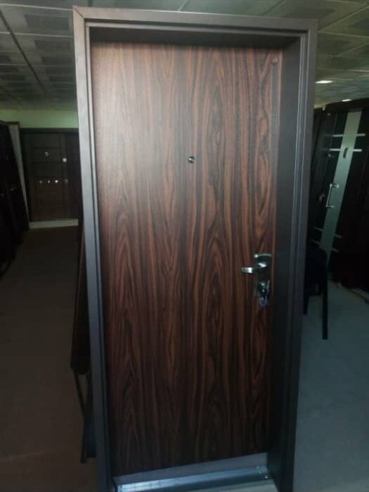 A modern single Israeli security door with a dark brown wood grain finish. The door has a black metal frame and a silver handle with a keyhole.